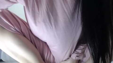 Media: Video of a woman in a light pink dress, bending over, with long black hair partially covering her face, taken from a low angle, emphasizing her curves and the fabric texture of her dress.