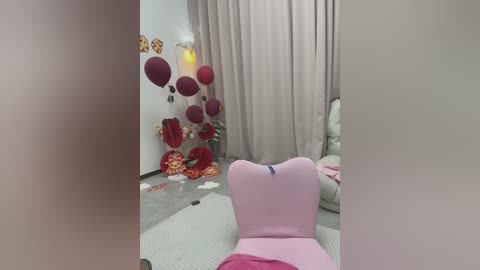 Video of a pink chaise lounge in a pastel-themed room with beige curtains, a bouquet of red roses, and heart-shaped balloons.