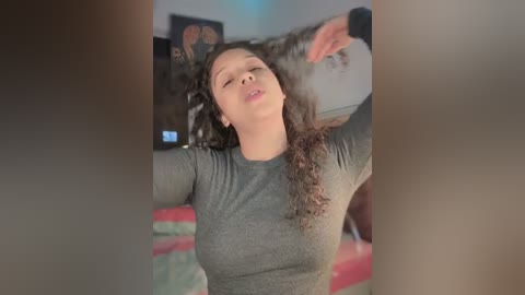 Media: Video of a light-skinned woman with curly hair, wearing a gray shirt, dancing in a living room with a couch and framed art on the wall.