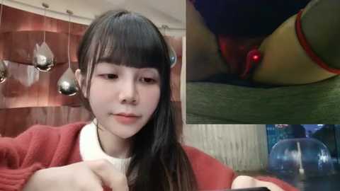 Media: Video of a young Asian woman with long black hair, wearing a red sweater, sitting indoors with a wooden table, surrounded by metallic pendant lights, and a close-up of a man's penis entering her.