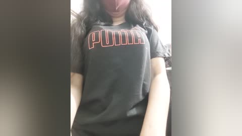 Media: Video of a person wearing a black \"Punkie\" t-shirt with red lettering, partially obscured by a red mask, standing indoors with blurred background.