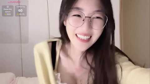 Media: A video of an East Asian woman with long black hair, glasses, and a yellow sweater, smiling broadly. The background shows a white wall with a digital display showing 60% fullness.