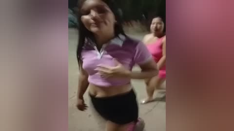 Media: Video of two women, one in a purple polo and black shorts, the other in a pink sports bra and shorts, walking on a dimly lit sidewalk.