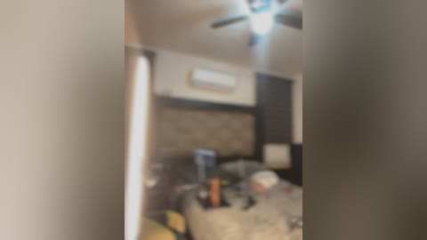 A blurry video of a messy bedroom with an air conditioner on the wall, a fan on the ceiling, and scattered items on the bed.