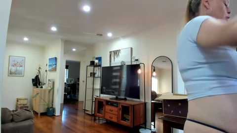 Media: Video of a modern, minimalist living room with hardwood floors, a TV stand, and a woman in a light blue shirt, standing and facing away.