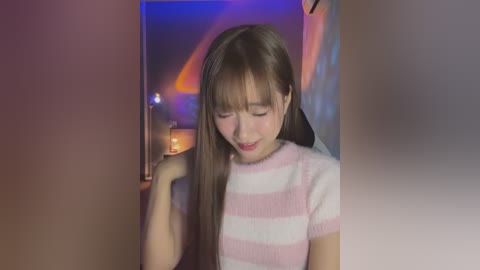 Video of a young Asian woman with long, straight brown hair, wearing a pink and white striped sweater, sitting in a dimly lit room with soft, purple and orange lighting.