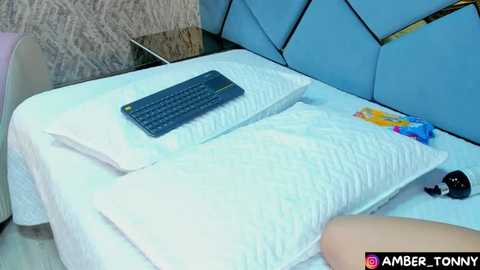 Media: Video of a modern bedroom with a blue headboard, a white pillow with a black keyboard on top, and a colorful candy wrapper on the bed.