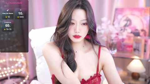 Media: Video of a young Asian woman with long, wavy black hair, wearing red lace lingerie, in a cozy bedroom with soft lighting and decor.