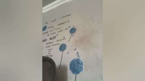 Video of a beige wall with a colorful, textured, blue dandelion wall decal and a white trim. Words like \"LOVE,\" \"FAMILY,\" and \"ALOT\" are written around it.