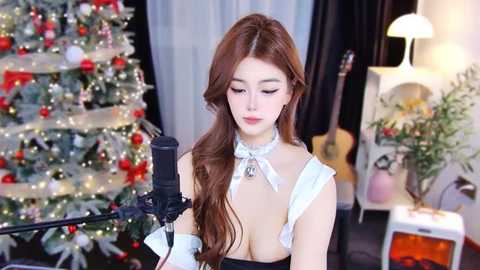 Media: A video of a fair-skinned, long-haired woman with large breasts in a revealing black and white maid outfit singing into a microphone in a festive room with a decorated Christmas tree and guitar.