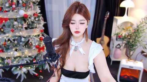 Media: Video of an Asian woman with long red hair in a black-and-white maid outfit singing into a microphone, surrounded by a festive Christmas tree and guitar, with a warm, cozy room in the background.