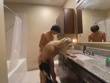 Media: Video of a nude couple having sex in a modern bathroom with beige walls, granite countertops, and a white bathtub.