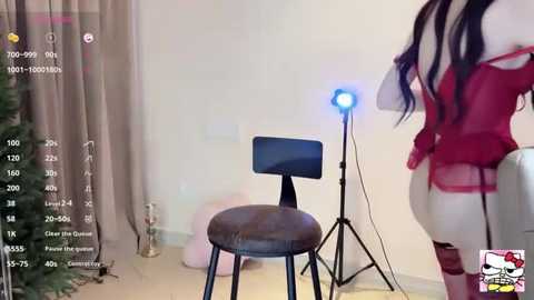 Media: A video shows a woman in a red lingerie outfit standing next to a stool in a dimly lit room. The background includes a Christmas tree and a studio light.