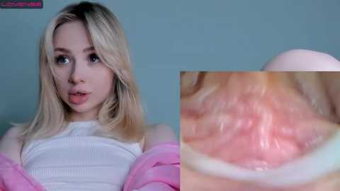 Media: Video of a blonde Caucasian woman with a pink jacket, white ribbed top, and light blue background. Close-up of her mouth and throat showing oral and pharyngeal tissues.