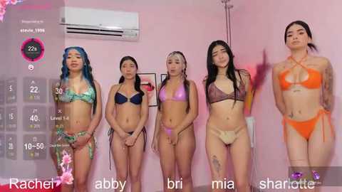 Video of five young Asian women in revealing bikinis standing against a pink wall, showing off their tanned skin, tattoos, and diverse body types.