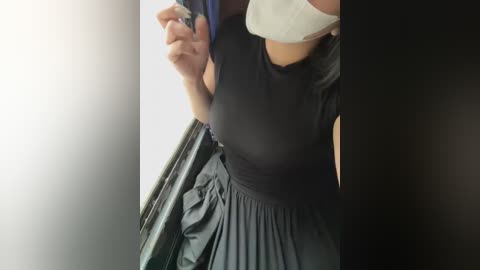 Media: Video of a person wearing a black dress, white face mask, and blue hairband, holding a phone, indoors, blurry background.