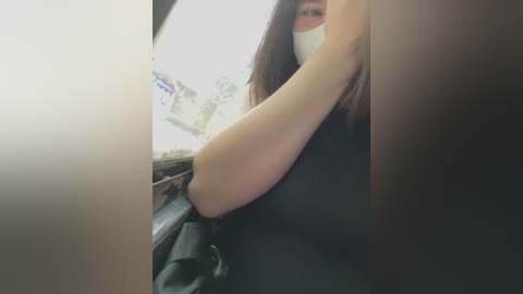 Media: A blurred video shows a person with long brown hair, wearing a white face mask, black top, and black jacket, holding a phone in a dimly lit car interior.