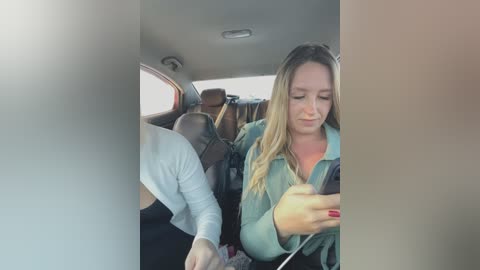 Media: Video of a woman with long blonde hair, wearing a green shirt, using a smartphone while sitting in a car.