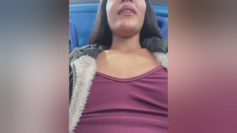 Media: A close-up video of a woman with medium-dark skin, wearing a purple tank top and a grey hoodie, reclining in a blue car seat. Her long black hair cascades over her shoulders.