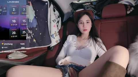 Media: Video of a young Asian woman with long black hair, wearing a white blouse and denim shorts, seated in a car, with a smartphone screen displaying live stream details in the background.