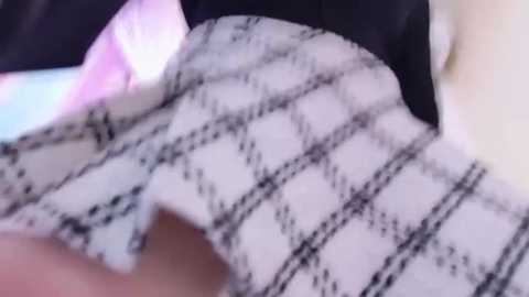 Media: Video of a close-up, blurred scene featuring a white, checkered-patterned cloth with black lines, possibly a tablecloth or napkin, partially covering a person's face. Background includes a mix of dark and light colors.