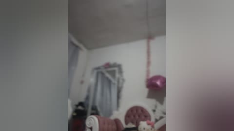 Media: A blurred video of a cluttered bedroom with a bed, pink lamp, and a stuffed toy on the floor. The walls are white, and a pink cat toy hangs from the ceiling.