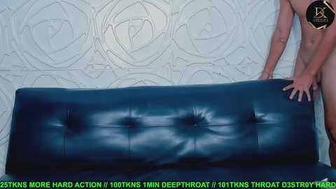 Media: A video depicts a nude man with a muscular build, light skin, and a tattoo on his left arm, leaning on a dark blue leather couch against a textured, pale green wall. Text overlays the image with instructions for a deep tissue massage.