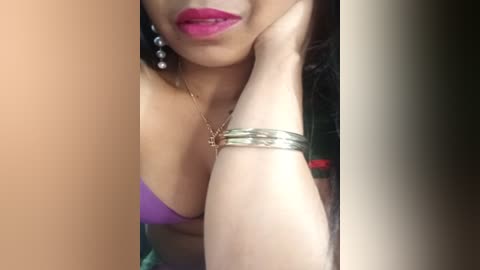 Media: Video of a woman with medium skin tone, wearing a purple strapless dress, silver bracelets, and bold pink lipstick. Her partially cropped face and arm are in focus.