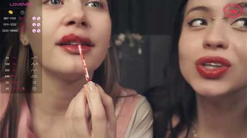 Media: A video captures two young women, one with red lipstick, applying it to the other's lips. The background is dark, with a virtual camera interface on the left.