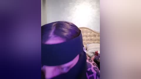 Media: A video captures a person with dark hair and a black mask, standing in a dimly lit bedroom with a leopard-print blanket and a tufted headboard.