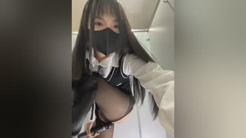 Media: Video of an Asian woman in a black face mask and revealing black outfit with white trim, performing a provocative pose in a dimly lit bathroom.