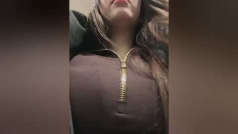 Media: A video of a woman with fair skin and brown hair, wearing a dark, unzipped hoodie, with a gold zipper visible. The image is blurred and grainy.