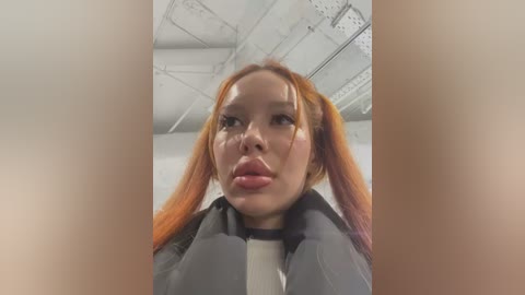 Media: Video of a young Asian woman with fair skin, wearing a black jacket, and orange pigtails. She has a neutral expression, taken from a low angle, inside an industrial warehouse with exposed metal beams.