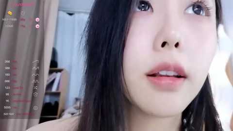 Media: A close-up video of an Asian woman with long, straight black hair, fair skin, and light makeup, wearing a pink top, taken indoors with blurred background.