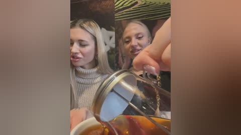 Media: Video of two young Caucasian women in a dimly lit cafe, one pouring tea from a teapot into a glass, wearing light sweaters.