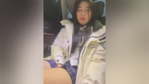 Media: Video of an Asian woman with long black hair, wearing a white jacket and plaid skirt, slumped in a car seat, eyes closed, mouth open.