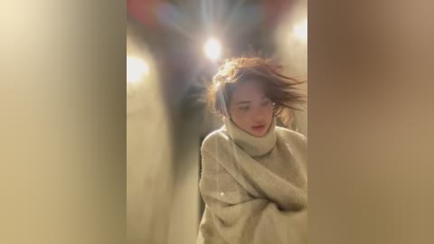 Media: Video of a young woman with fair skin, red hair, and a pale beige turtleneck sweater, walking through a dimly lit, narrow corridor with warm, ambient light and a slight lens flare.