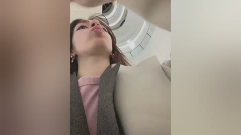 Media: A low-angle video captures a woman in a grey blazer and pink top, with dark hair, looking up in an airplane, focusing on the overhead compartment.