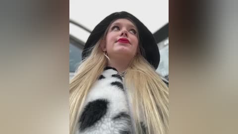 Media: Video of a young woman with long blonde hair, wearing a black hat and a cow-patterned coat, looking up at the sky.