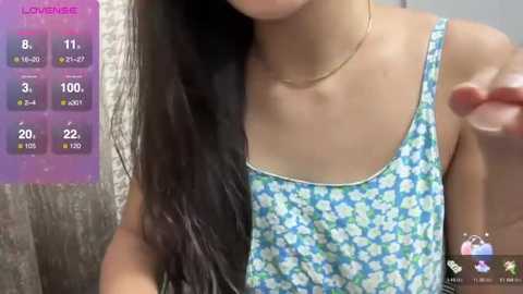 Media: Video of an Asian woman with long black hair, wearing a blue floral-patterned tank top, indoors, with a purple background displaying temperature and humidity levels.