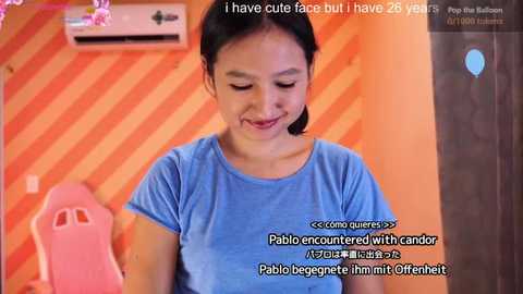 Video of a young Asian girl with black hair, smiling, wearing a light blue shirt, standing in an orange-striped room with a pink chair. Text overlay mentions facial filters and age.