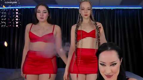 Media: A video featuring two young women in matching red lingerie and garter belts, one with long braids, standing against a dark backdrop.