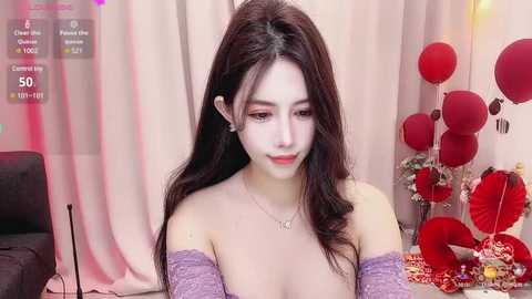 Media: Video of a young Asian woman with long black hair, wearing a purple off-shoulder top, seated in a room with red balloons and floral arrangements.