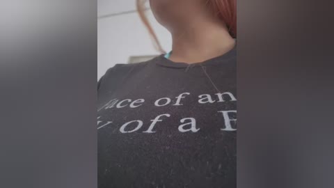 Media: Video of a woman wearing a dark gray T-shirt with white text that reads, \"Once upon a time.\" The background is blurry, featuring a white wall. Her red hair is visible.