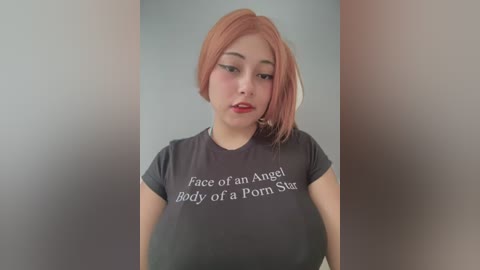 Media: Video of a young woman with light skin and shoulder-length, dyed pink hair, wearing a black t-shirt with white text: \"Face of an Angel Body of a Porn Star.\