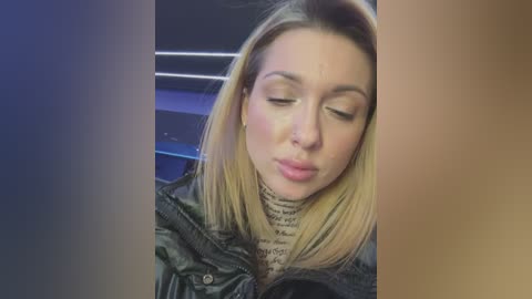 Media: Video of a blonde woman with straight hair, wearing a black jacket and a light-colored turtleneck, making a smooching face, set against a dark background with blue and brown gradients.