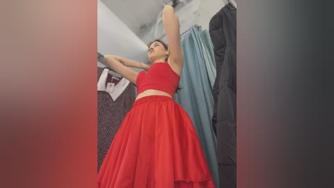 Media: Video of a woman with light skin and dark hair, wearing a sleeveless red dress, reaching for a blue garment in a clothing store, surrounded by racks of clothes.