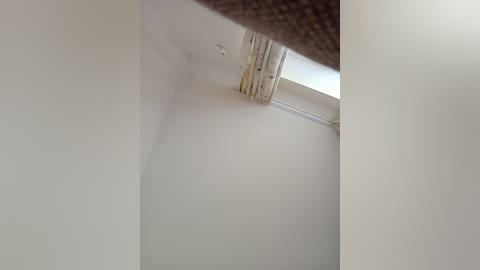 Media: Video of a beige ceiling with a white window frame, partially covered by a beige curtain. The image focuses on the top corner of the window, emphasizing the clean, minimalist interior design.