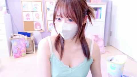 Media: A video of an East Asian woman in a pastel room, wearing a light blue camisole and a white mask, with straight brown hair tied into pigtails.