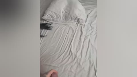 Media: Video of a person in bed, with wrinkled white sheets and a pillow, partially visible hand at the bottom. Soft lighting, minimalist bedroom setting.